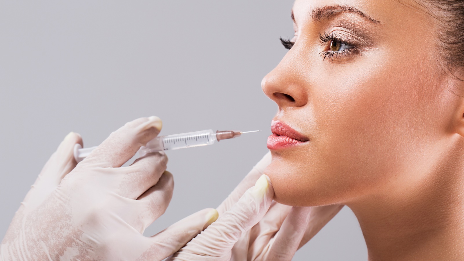 A lip filler practitioner is about to inject a young woman with dermal filler.