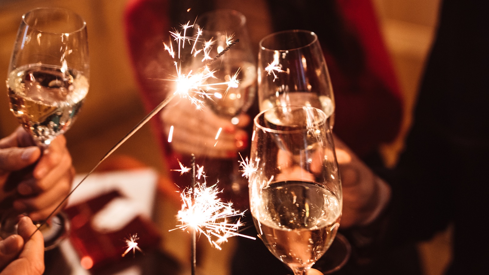 A group of people hold glasses of wine and sparklers during a holiday party.