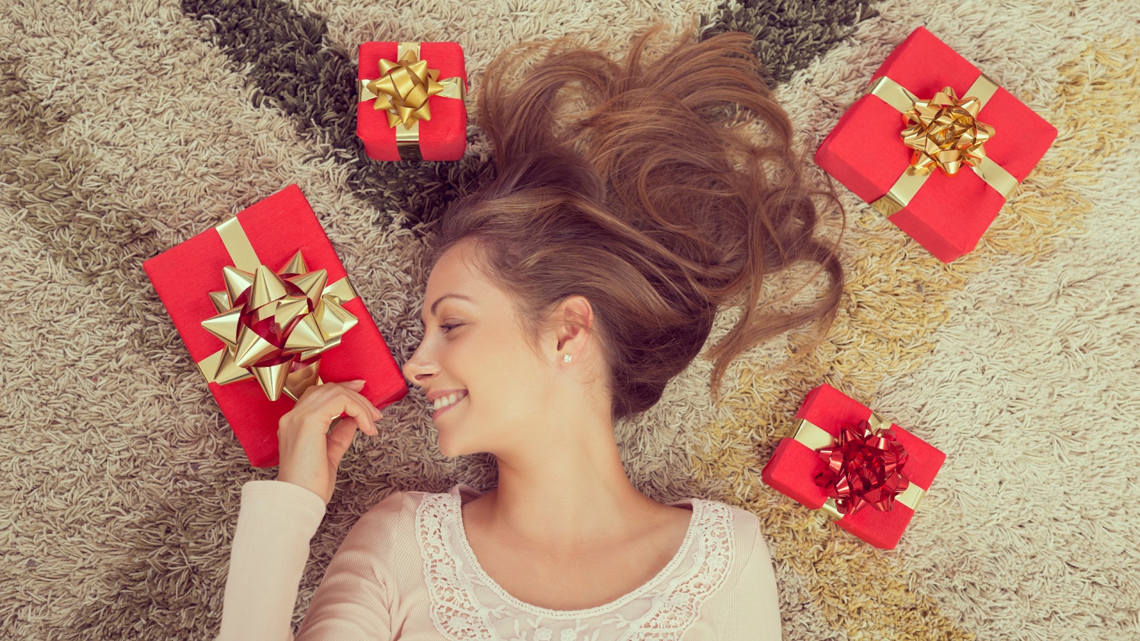 A woman with smooth skin lies in a pile of gifts, smiling.