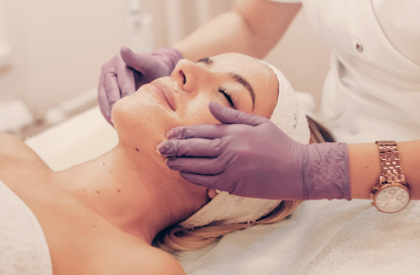 A practitioner wearing gloves applies a chemical on a female patient’s face.