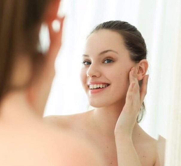 A woman examines her clear, radiant skin in the mirror, free from age spots.