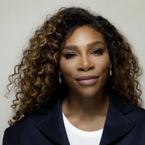 A close-up of Serena Williams, wearing a blazer and white T-shirt, posing for a camera.