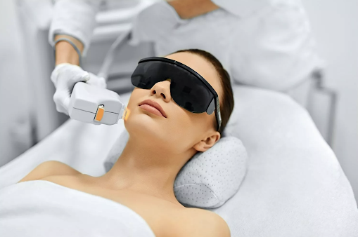 A woman with black shades laying on a white bed with receives a laser treatment.